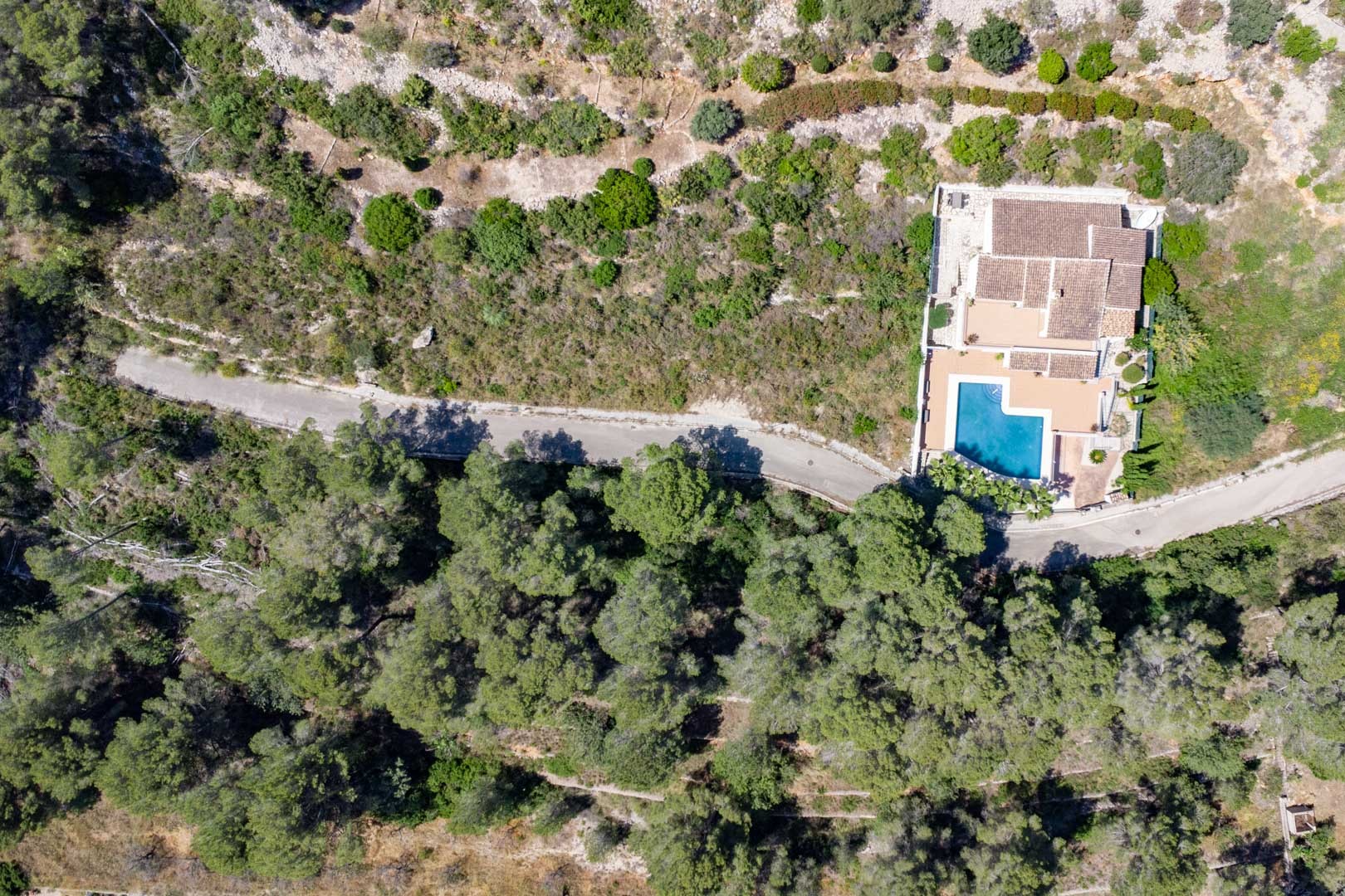 Luftbild einer Villa mit L-förmigem Pool und Ziegeldach, eingebettet in eine natürliche Waldlandschaft mit mediterraner Vegetation in Alcalalí.