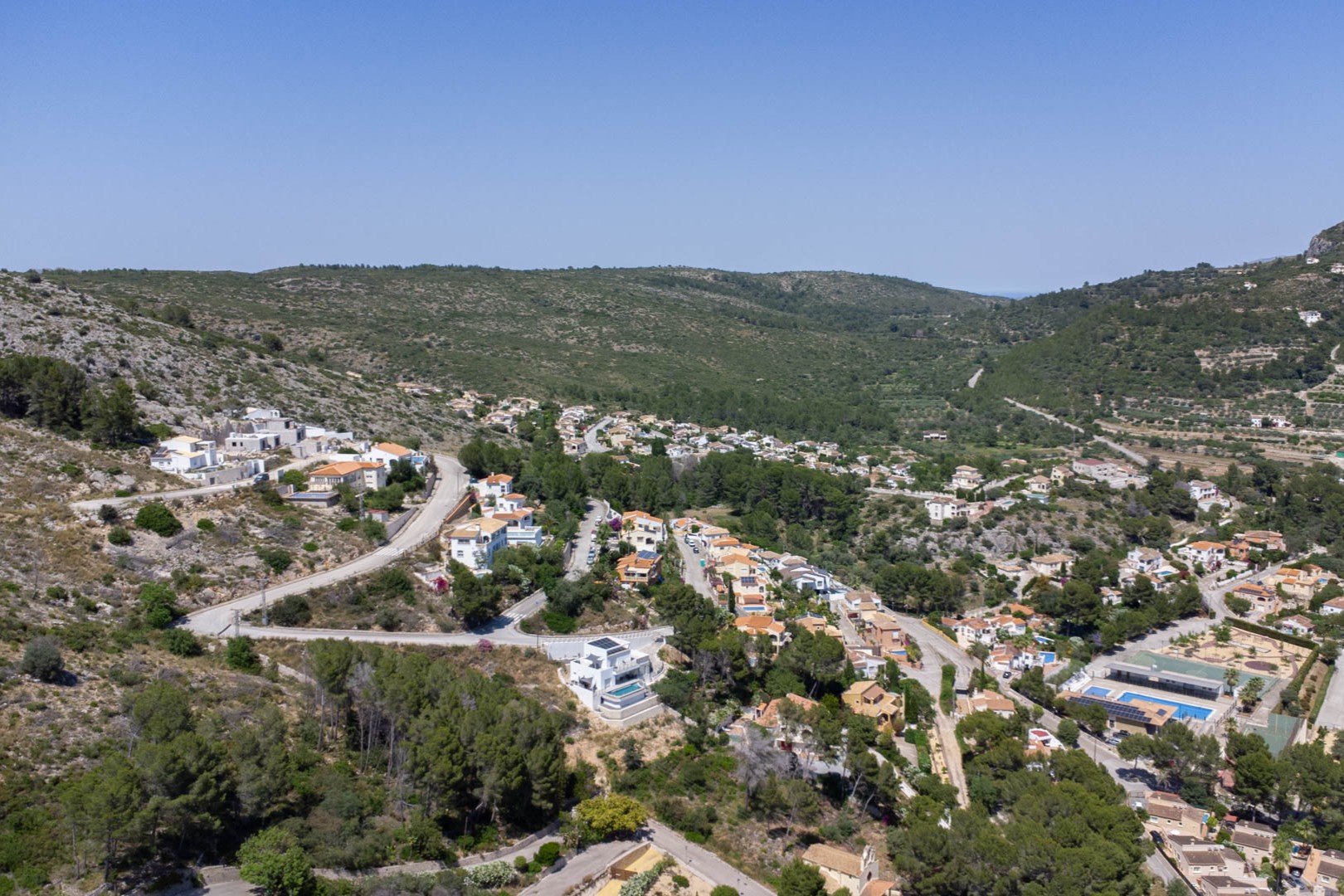 Panorama-Luftaufnahme des Wohngebiets VALL DE POP in Alcalalí, die die erhöhte Lage der Grundstücke und deren Einbettung in die natürliche Tallandschaft zeigt.