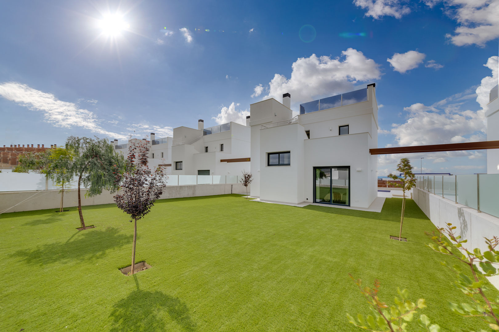 Außenansicht der Villa mit minimalistischer weißer Fassade, weitläufigem Rasengarten und Dachterrassen mit Glasgeländern.