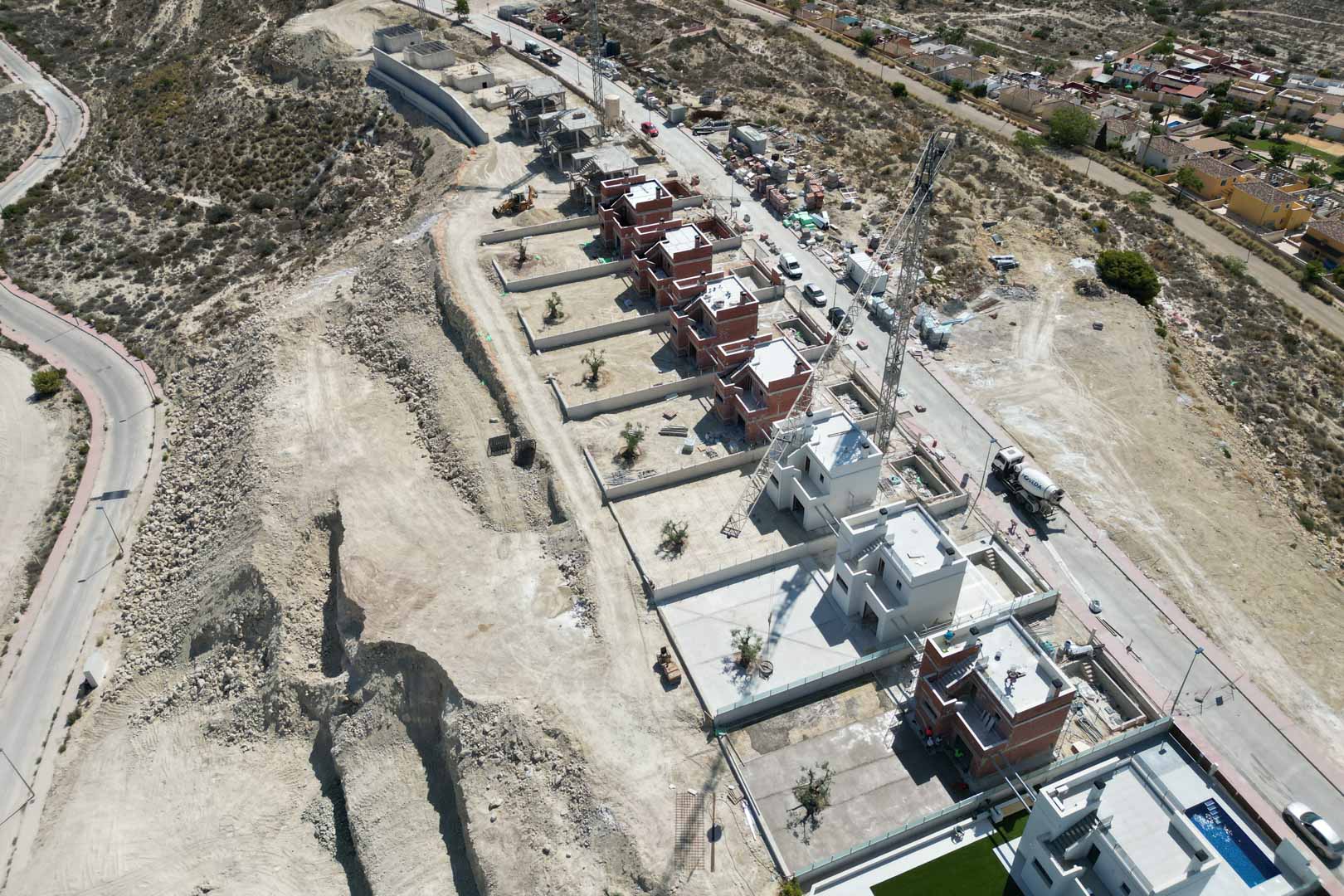 Luftaufnahme der Villenanlage in der Bauphase, die die erhöhte Hanglage und die Anordnung der modernen, freistehenden Gebäudestrukturen zeigt.