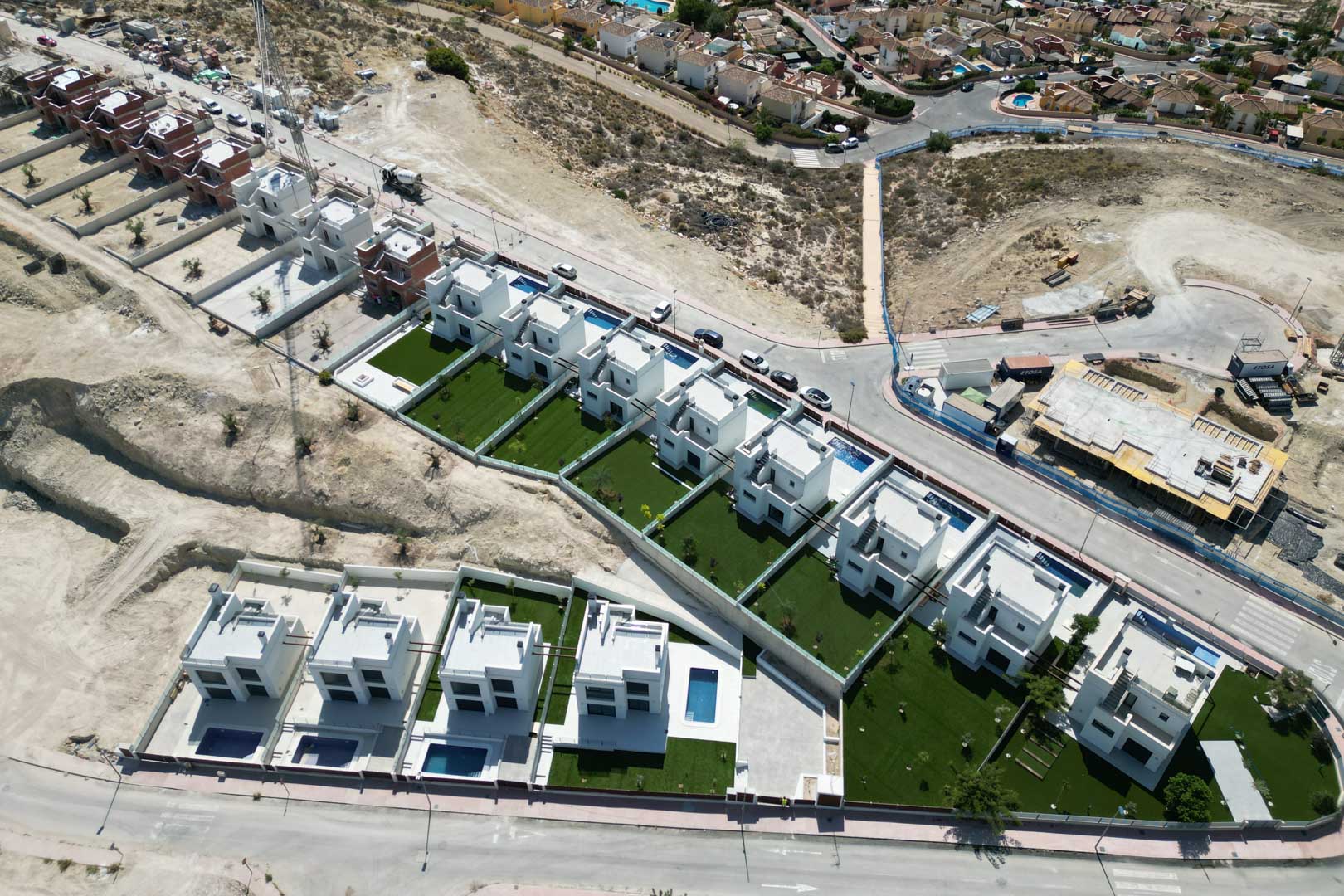 Luftaufnahme einer modernen Wohnanlage mit weißen Villen, privaten Pools und angelegten Gärten in erhöhter Hanglage.