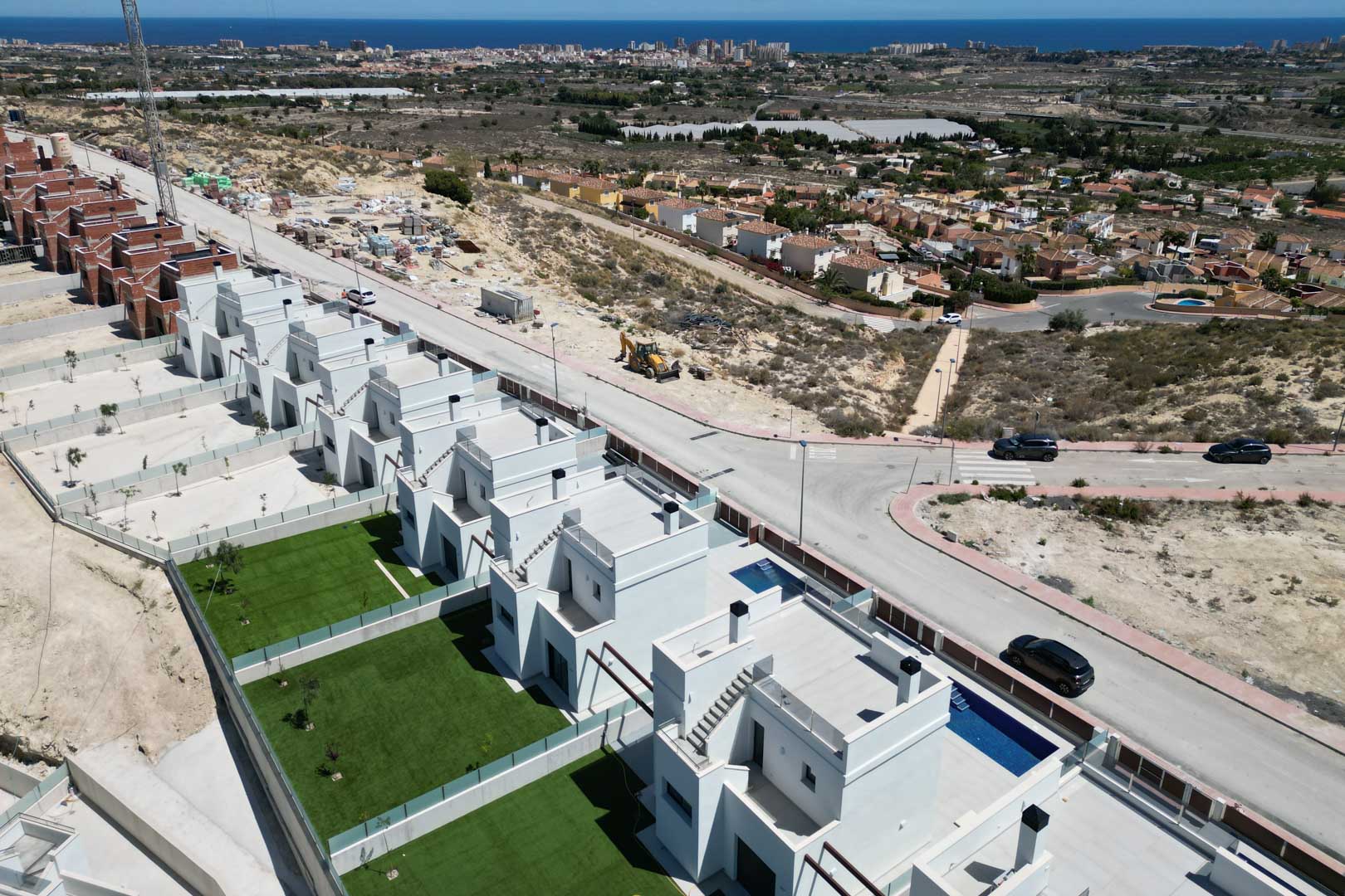 Luftaufnahme moderner Villen mit Privatgärten, Pools und Dachterrassen in Hanglage, die einen weiten Blick über die Küste und das Mittelmeer bietet.