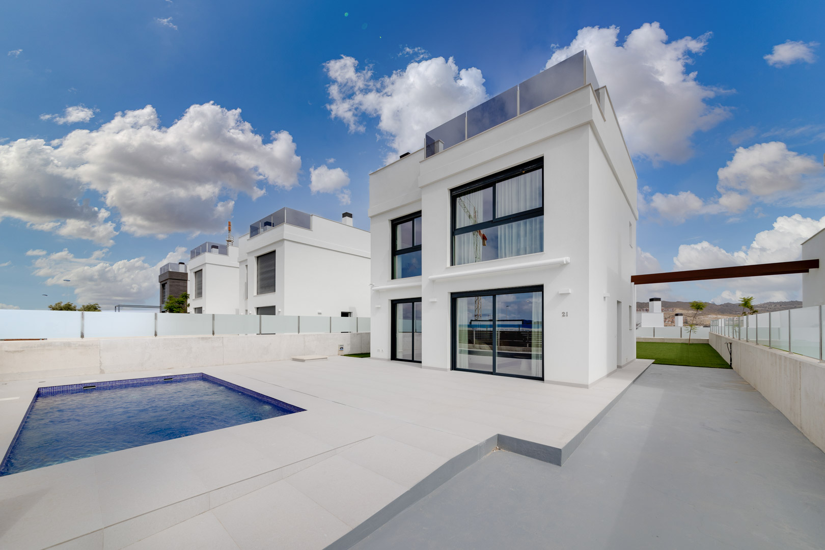 Moderne weiße Villa mit privatem rechteckigem Pool, großzügiger Fliesenterrasse und großen Fensterfronten in minimalistischem Design.