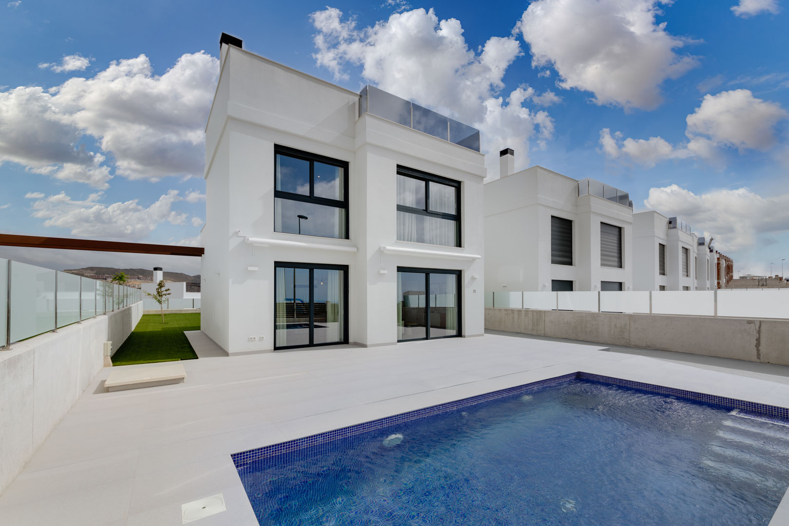 Moderne weiße Villa mit schwarzen Fensterrahmen, großzügiger Fliesenterrasse und privatem Pool mit blauen Mosaikfliesen.