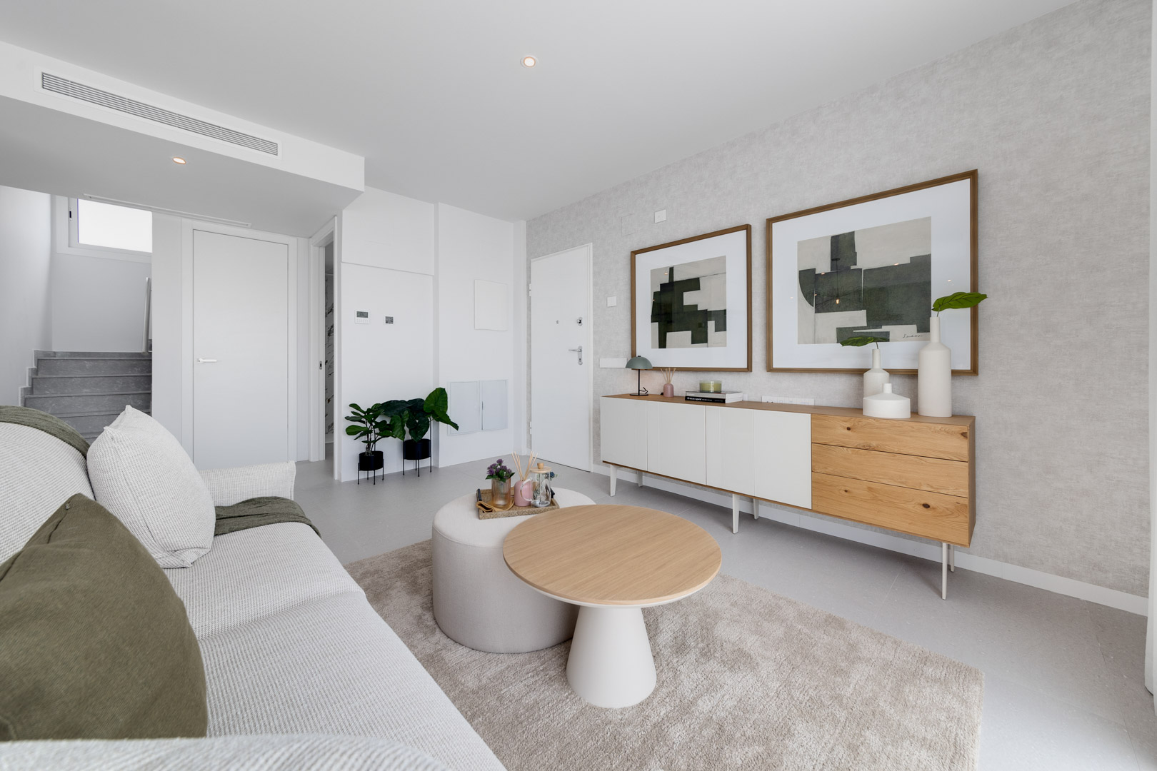 Moderner Wohnbereich mit minimalistischem Sideboard, abstrakter Kunst und einer gemütlichen Sitzecke in neutralen Farben mit Holzdetails.