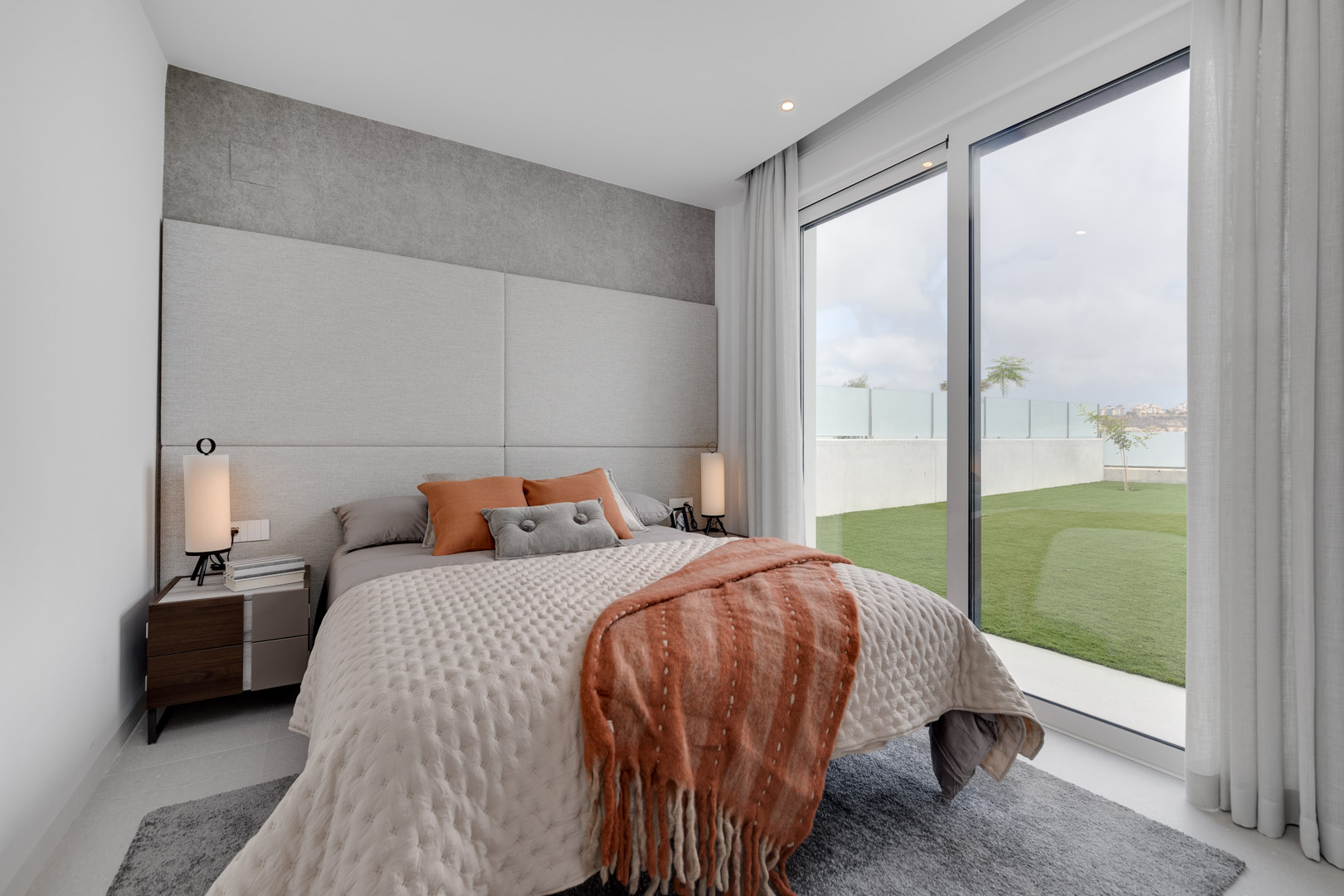 Modernes Schlafzimmer mit gepolstertem Kopfteil, Textilien in Erdtönen und bodentiefen Glastüren mit direktem Zugang zum privaten Garten.