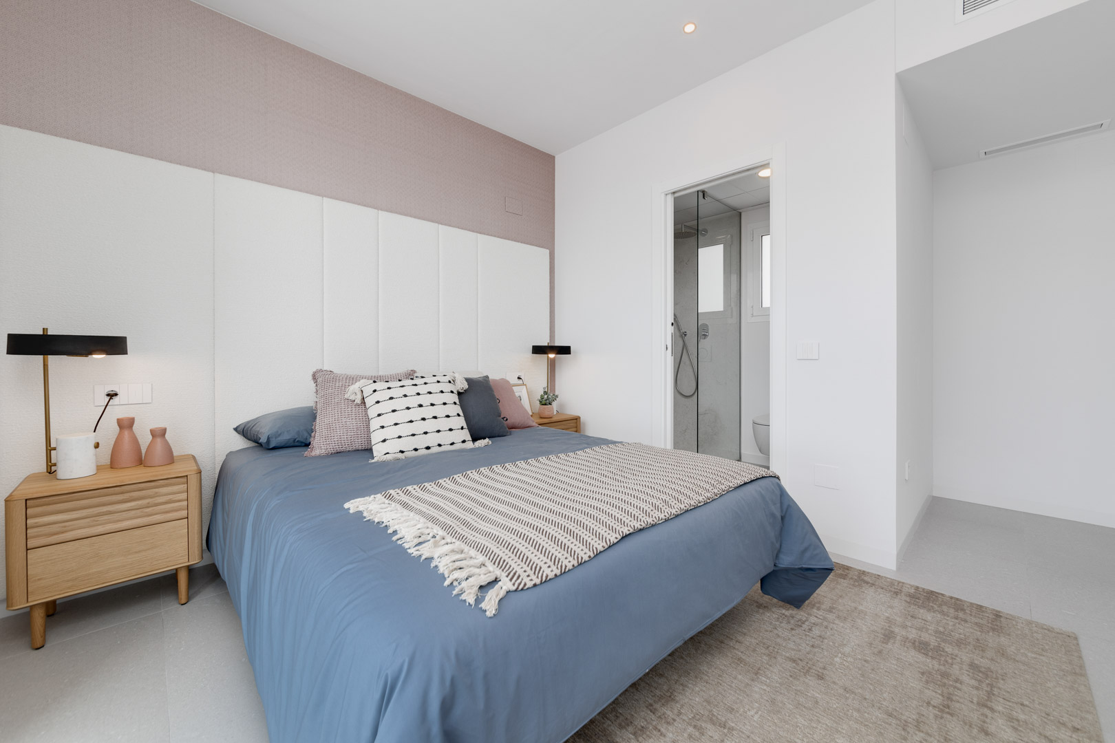 Modernes Schlafzimmer mit weißem Paneel-Kopfteil, malvenfarbener Akzentwand und integriertem En-Suite-Badezimmer mit Glastrennwand.