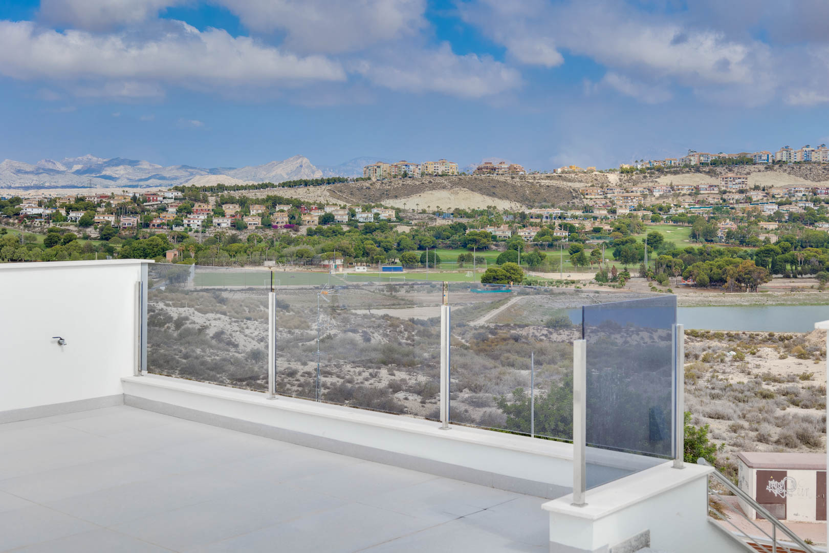 Obere Terrasse mit großformatigen grauen Fliesen und Glasgeländer, die einen Panoramablick auf die Berge, den See und die Golfplätze bietet.
