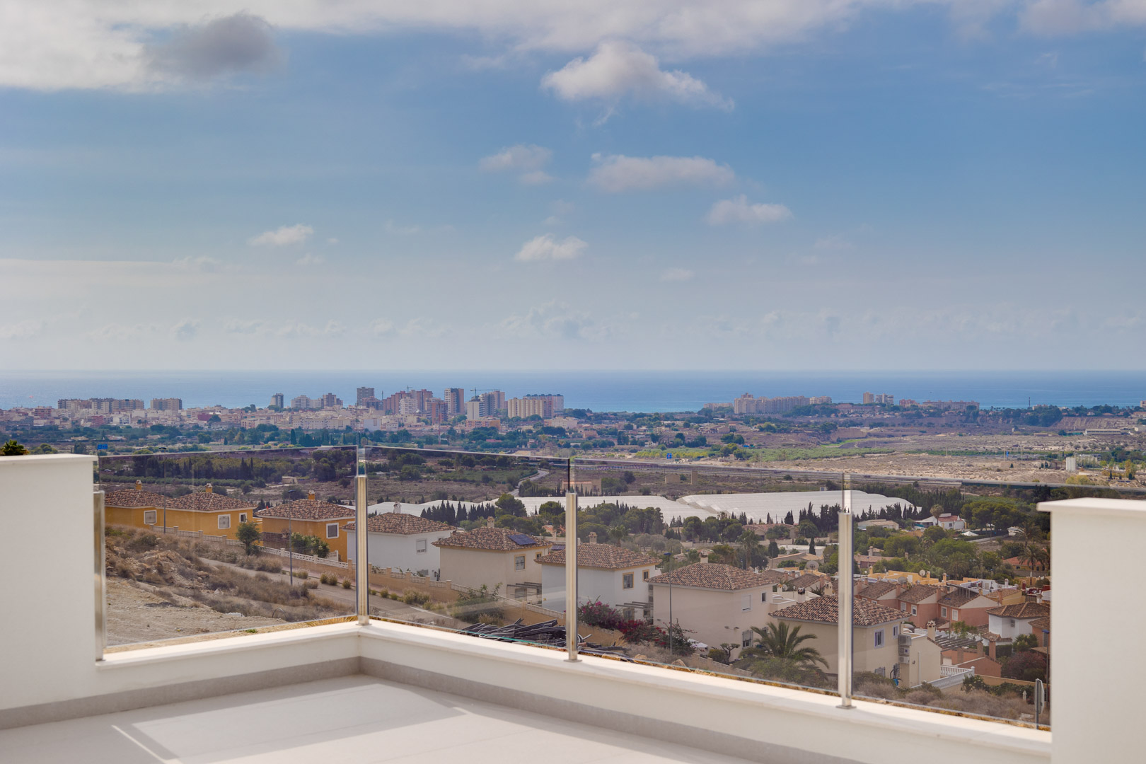 Obere Terrasse mit hellen Keramikfliesen und Glasbalustrade, die einen ungehinderten Panoramablick auf die Küste und das Mittelmeer bietet.