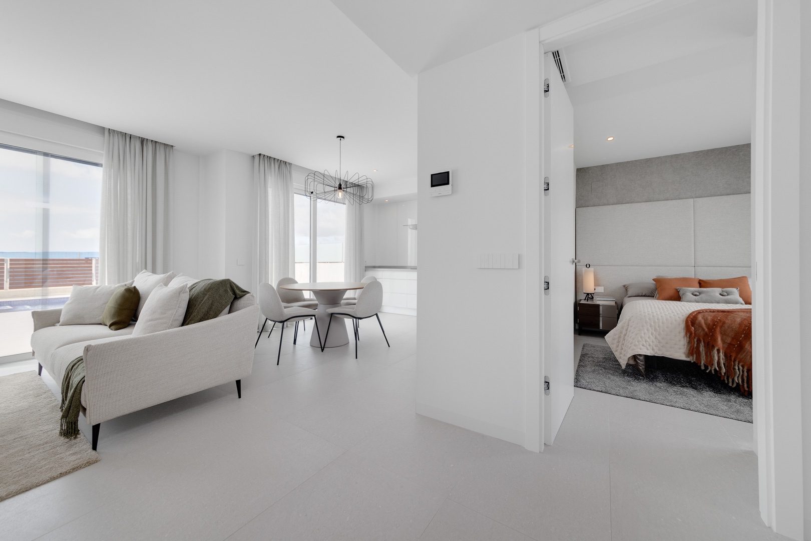 Offener Wohn- und Essbereich mit großformatigen Fliesen, Designer-Pendelleuchte und Blick in ein Schlafzimmer mit gepolstertem Kopfteil und warmen Akzenten.