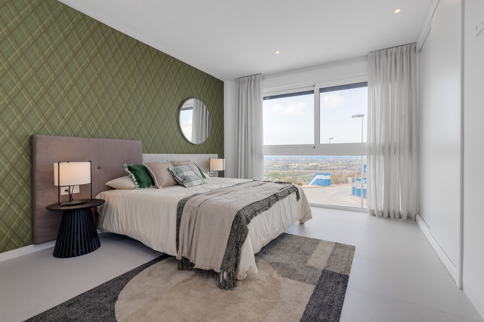 Schlafzimmer mit grüner Mustertapete, bodentiefem Fenster mit Weitblick und weißem Einbauschrank. Moderne Einbaustrahler und heller Fliesenboden ergänzen das Design.