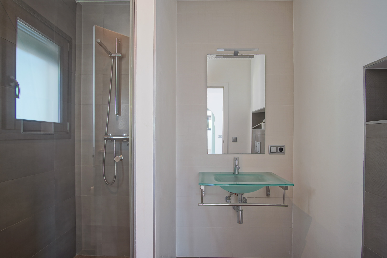 Modernes Badezimmer mit einem lichtdurchlässigen Glaswaschbecken, beleuchtetem Spiegel und einer begehbaren Dusche mit dunkelgrauen Fliesen und Glastrennwand.