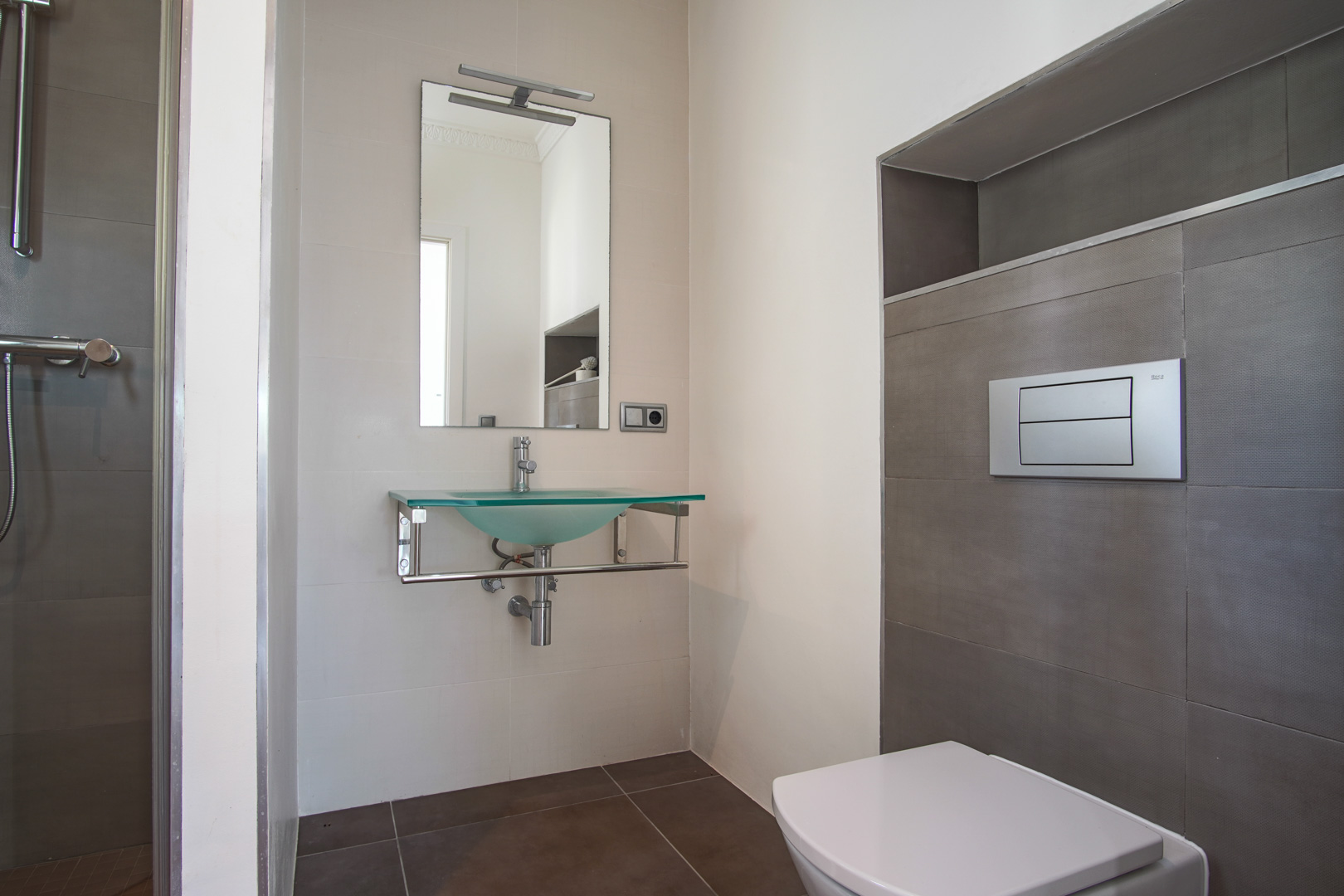 Modernes Badezimmer mit wandhängendem WC, Waschbecken aus satiniertem Glas auf Chromhalterung und strukturierten Fliesen mit integrierter Wandnische.