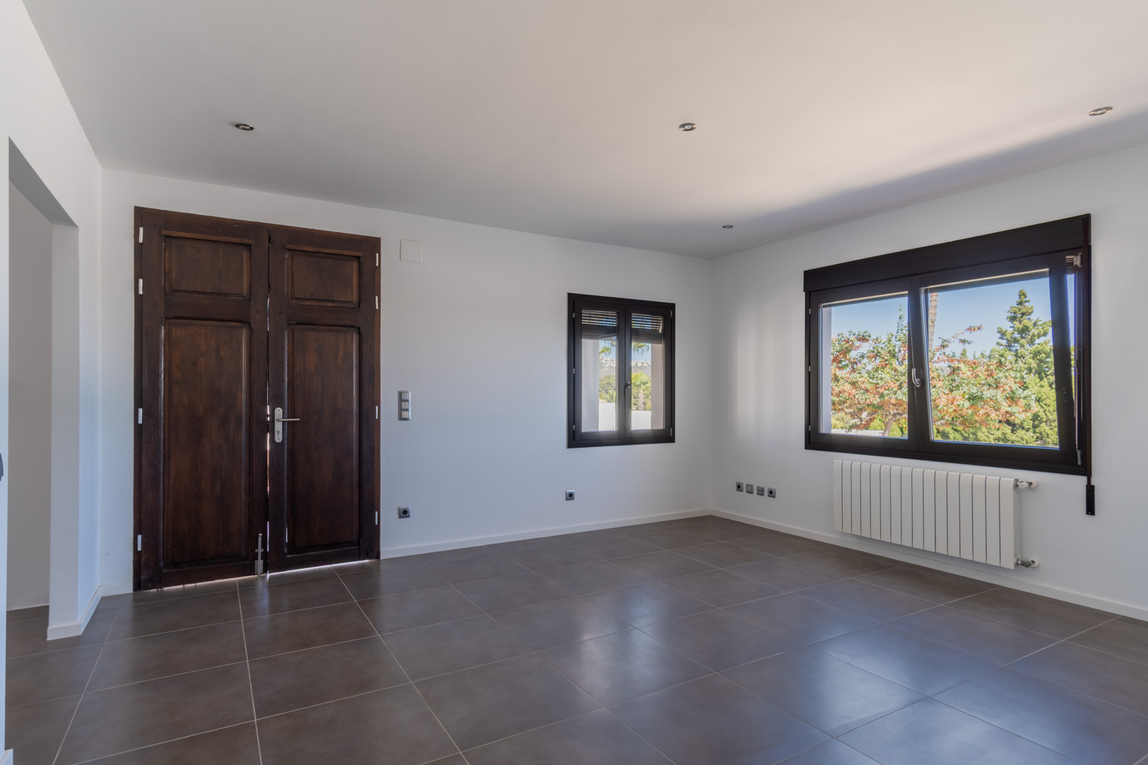Wohnbereich mit restaurierter antiker Holztür, Aluminiumfenstern in Holzoptik, Heizkörper und großformatigen grauen Bodenfliesen.