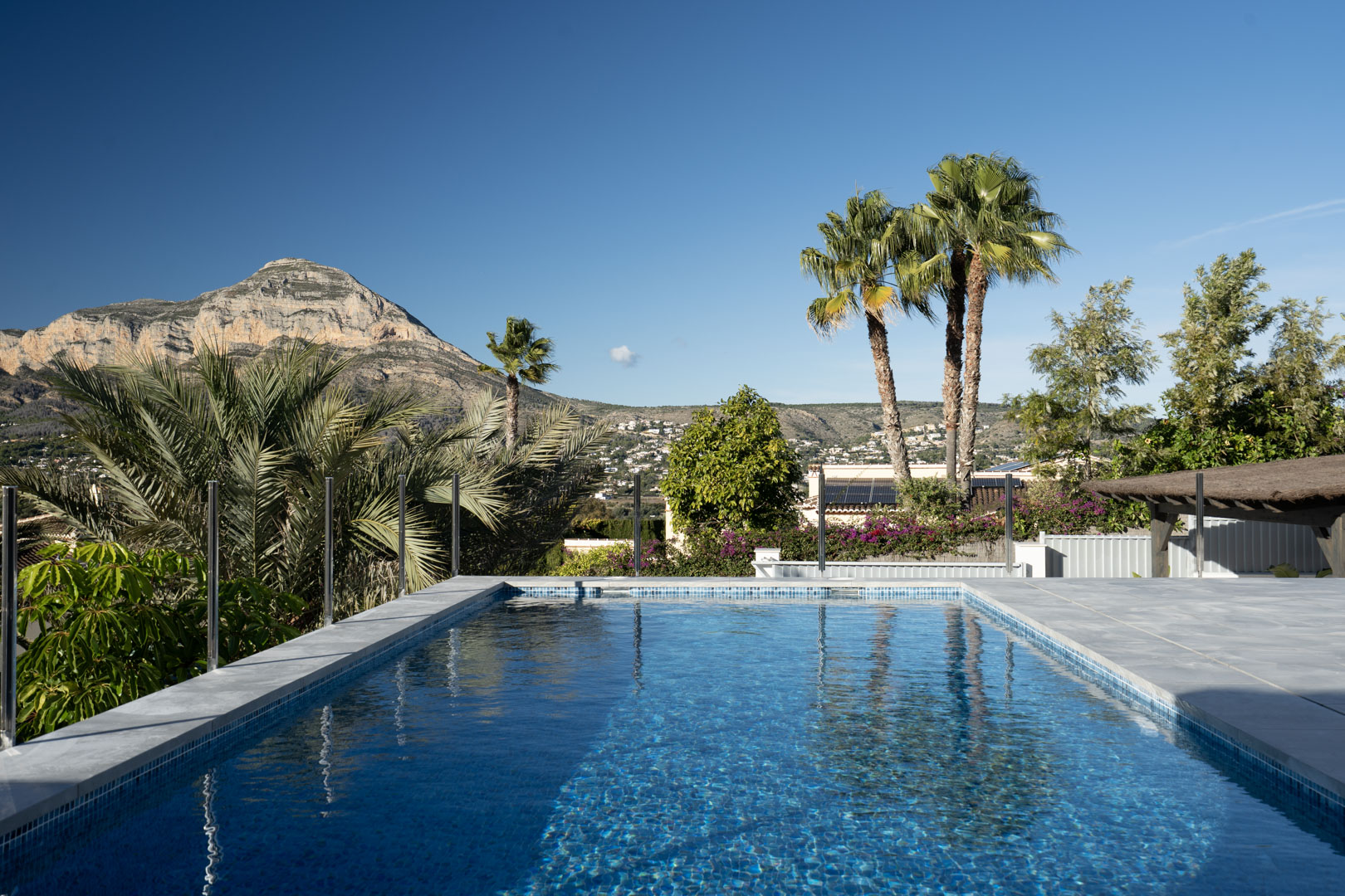 Blick auf den privaten Pool mit blauen Mosaiken, umgeben von Grün und mit einem majestätischen Berg im Hintergrund.