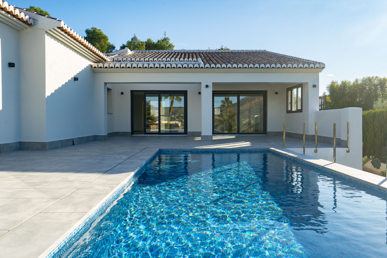 Blick auf den privaten Pool mit blauen Mosaikfliesen und die graue Fliesenterrasse der Villa.