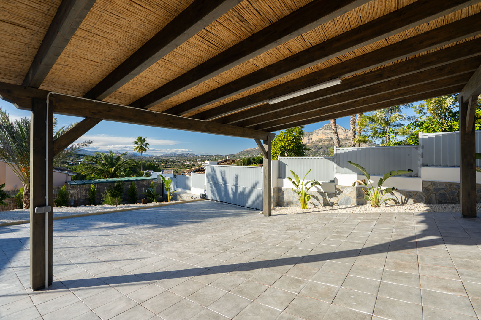 Pergola mit Schilfdecke und Fliesenboden, mit Blick auf Grün und Berge.
