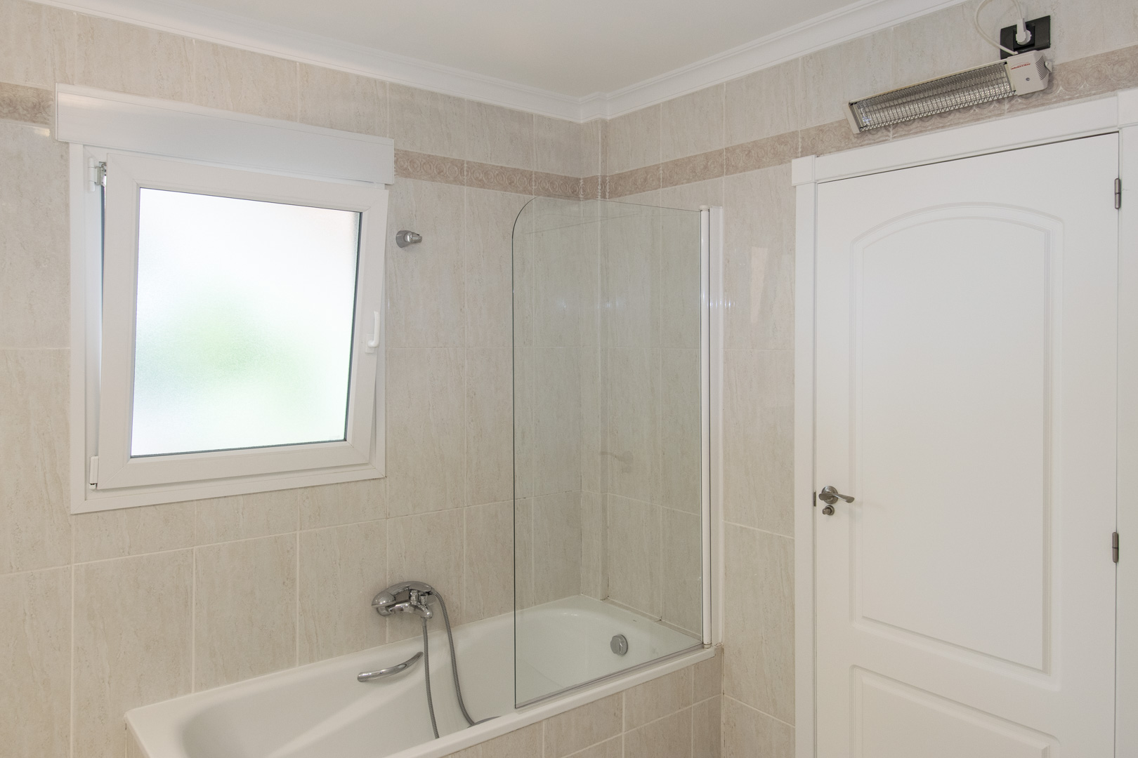 Badezimmer mit Badewanne und Glasduschwand, gefliesten Wänden mit dekorativer Bordüre, einem PVC-Fenster mit Sichtschutz und Wandheizgerät.