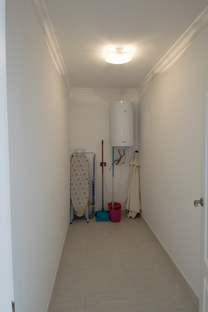 Funktionaler Hauswirtschaftsraum mit Elektro-Warmwasserspeicher, Stauraum für Reinigungsutensilien und Fliesenboden mit Deckenleisten.