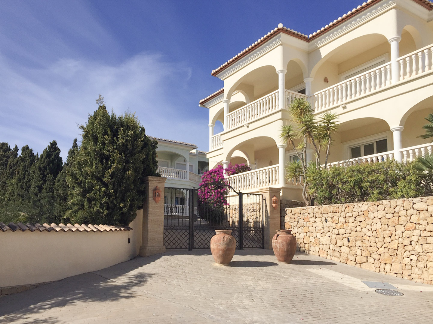 Haupteingang mit schmiedeeisernem Tor, Natursteinmauern und mediterraner Architektur mit Rundbogenterrassen und dekorativen Terrakotta-Amphoren.