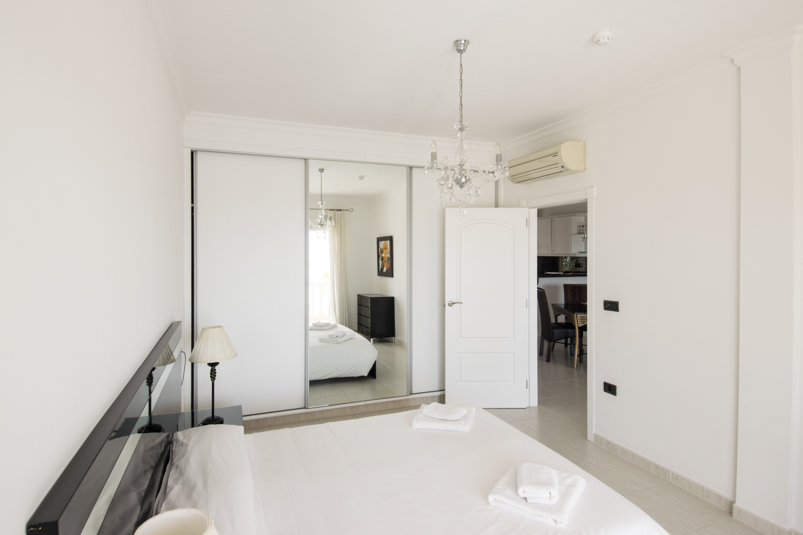 Hauptschlafzimmer mit Einbauschrank inklusive Spiegelschiebetür, Kristallkronleuchter und Split-Klimaanlage über dem Durchgang zum Wohnbereich.