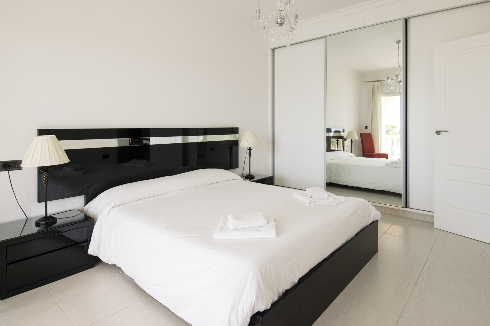 Hauptschlafzimmer mit schwarzem Lack-Kopfteil, passenden Nachttischen und einem großen Einbauschrank mit verspiegelten Schiebetüren und Kristallleuchter.