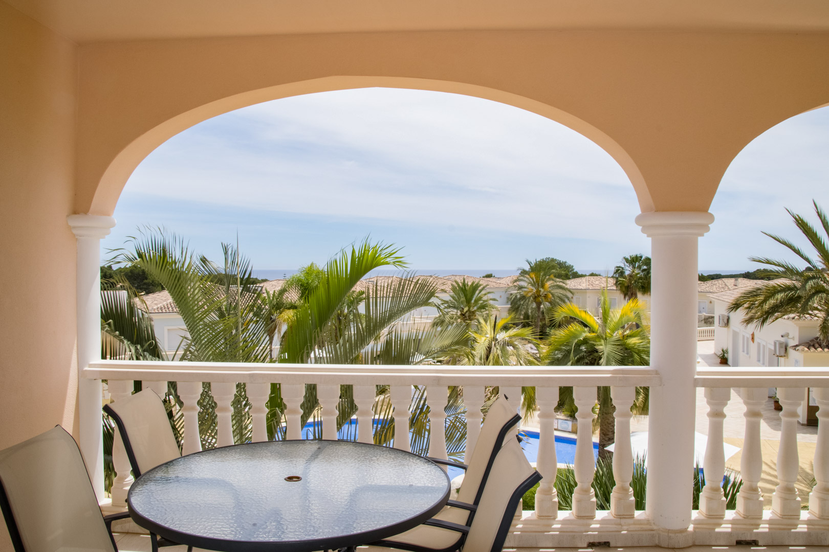 Überdachte Terrasse mit Rundbögen und Balustraden-Geländer. Der Außenbereich bietet einen Essplatz mit Blick auf die Palmenlandschaft, den Pool und das Meer.