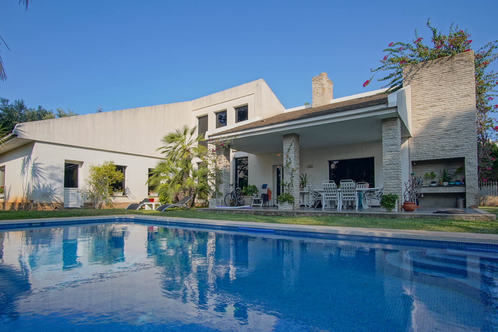 Außenansicht des privaten Pools und der überdachten Terrasse mit Steinsäulen, Essbereich im Freien und integrierter Grillstation im Garten.