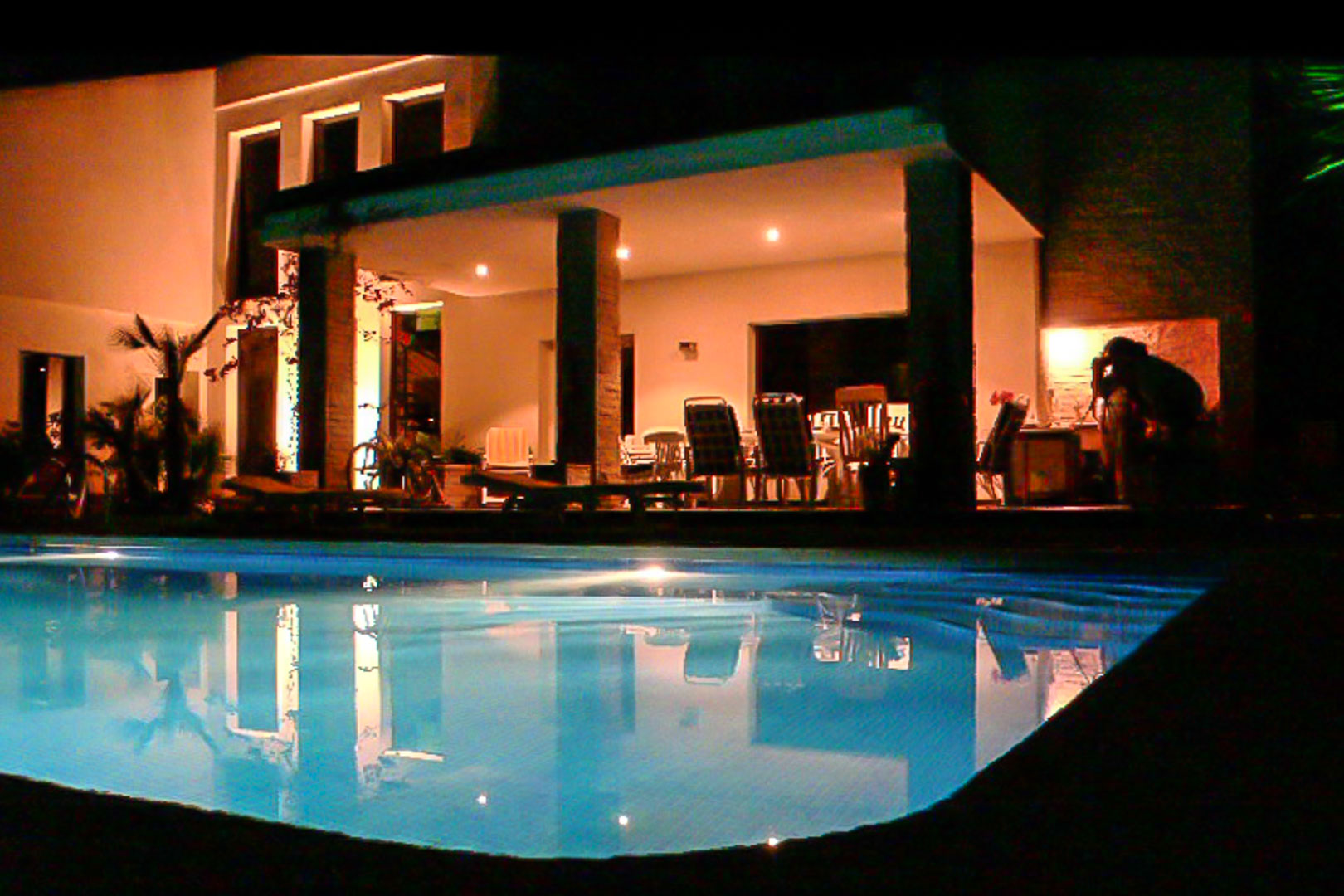 Beleuchtete überdachte Terrasse und privater Pool bei Nacht, mit steinverkleideten Säulen und einem integrierten Essbereich im Freien.