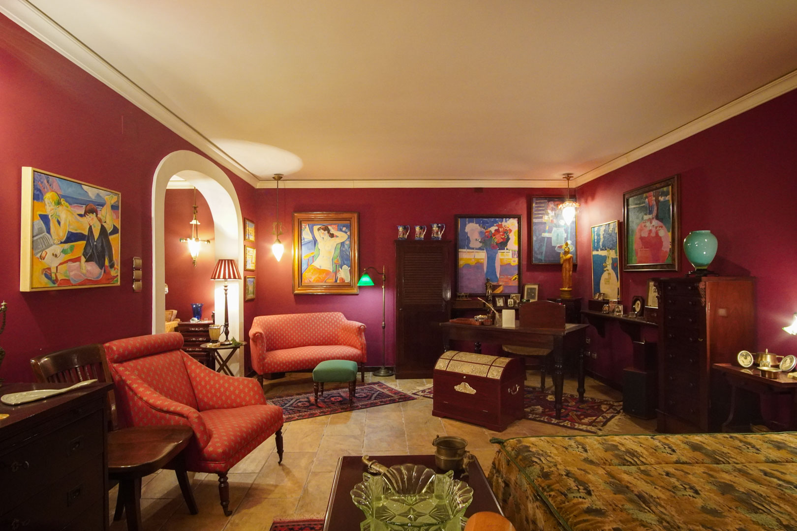 Klassischer Wohnbereich mit weinroten Wänden, Marmorböden und integriertem Arbeitsplatz. Kunstgemälde, antike Möbel und warme Beleuchtung prägen das elegante Ambiente.