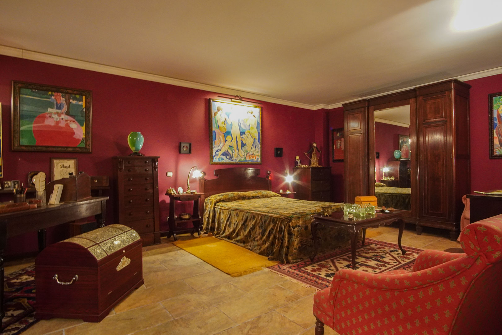 Klassisches Schlafzimmer mit burgunderroten Wänden, dunklen Massivholzmöbeln, Natursteinboden und einem großen Kleiderschrank mit Spiegel.