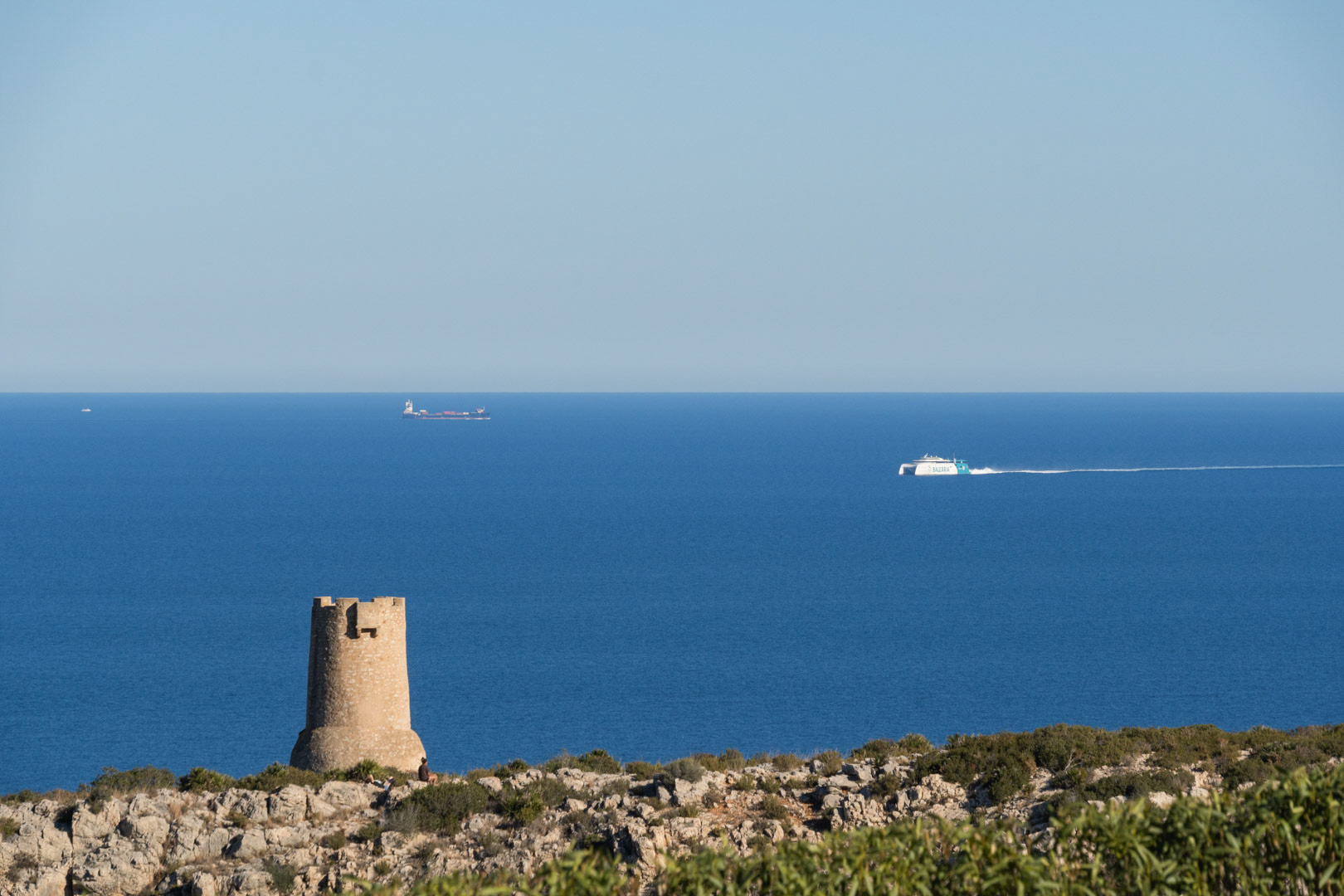 Panoramablick auf die Küste von Dénia mit dem historischen Wachturm Torre del Gerro und Fähren auf dem Mittelmeer in Richtung der Balearen.