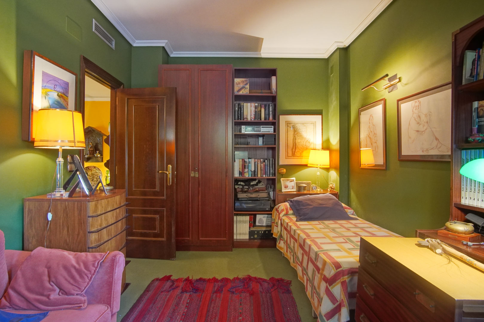 Schlafzimmer mit grünen Wänden, klassischen dunklen Holzmöbeln und Einzelbett. Ausgestattet mit Einbauregalen, warmer Beleuchtung und Kanalklimaanlage.