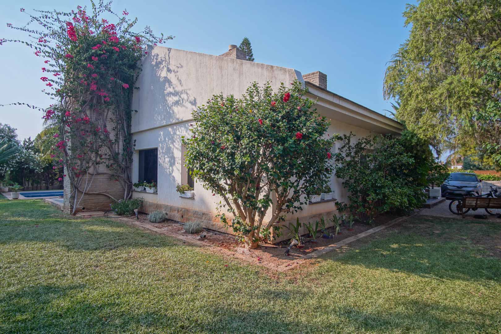 Seitenfassade der Villa mit Naturrasen, kletternder Bougainvillea an einer Natursteinwand und mediterranen Sträuchern im Garten.