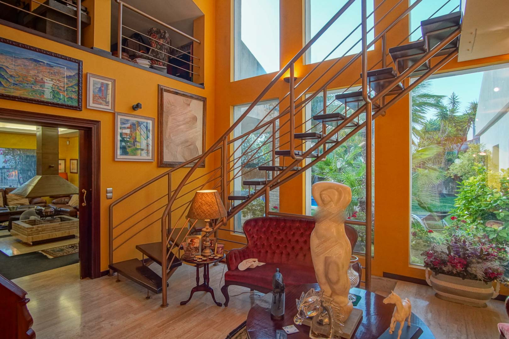 Wohnbereich mit doppelter Deckenhöhe, offener Treppe, großen Fensterfronten zum Garten und eleganten Marmorböden im gesamten Raum.