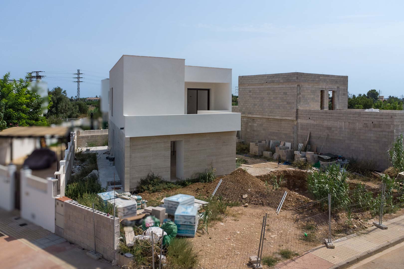 Außenansicht der im Bau befindlichen Villa mit Steinfassade im Erdgeschoss und weißem Obergeschoss. Die Ausgrabung für den privaten Pool ist bereits sichtbar.