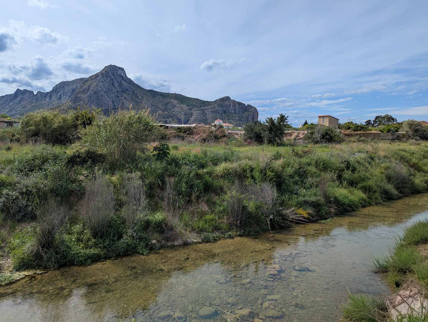Blick auf die natürliche Umgebung mit einem klaren Bachlauf und üppiger Vegetation vor der Kulisse der markanten Bergkette.