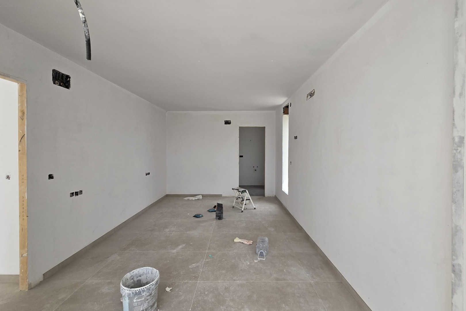 Innenansicht im Bau mit großformatigen Feinsteinzeugfliesen und glatten weißen Wänden. Sichtbare Elektrovorinstallationen und Durchgänge zu angrenzenden Räumen.