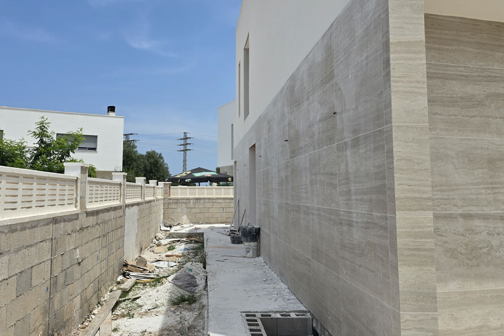 Seitenfassade im Bau mit großformatigen Steinoptik-Fliesen in Cremetönen, die die moderne Architektur und die Grundstücksbegrenzung verdeutlichen.