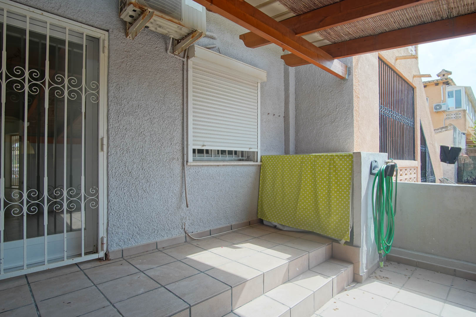 Außen-Terrasse mit Fliesenboden, Holzpergola mit Schilfrohrmatten und Sicherheitstür. Ausgestattet mit Klimaanlage und einem praktischen Außenbereich.