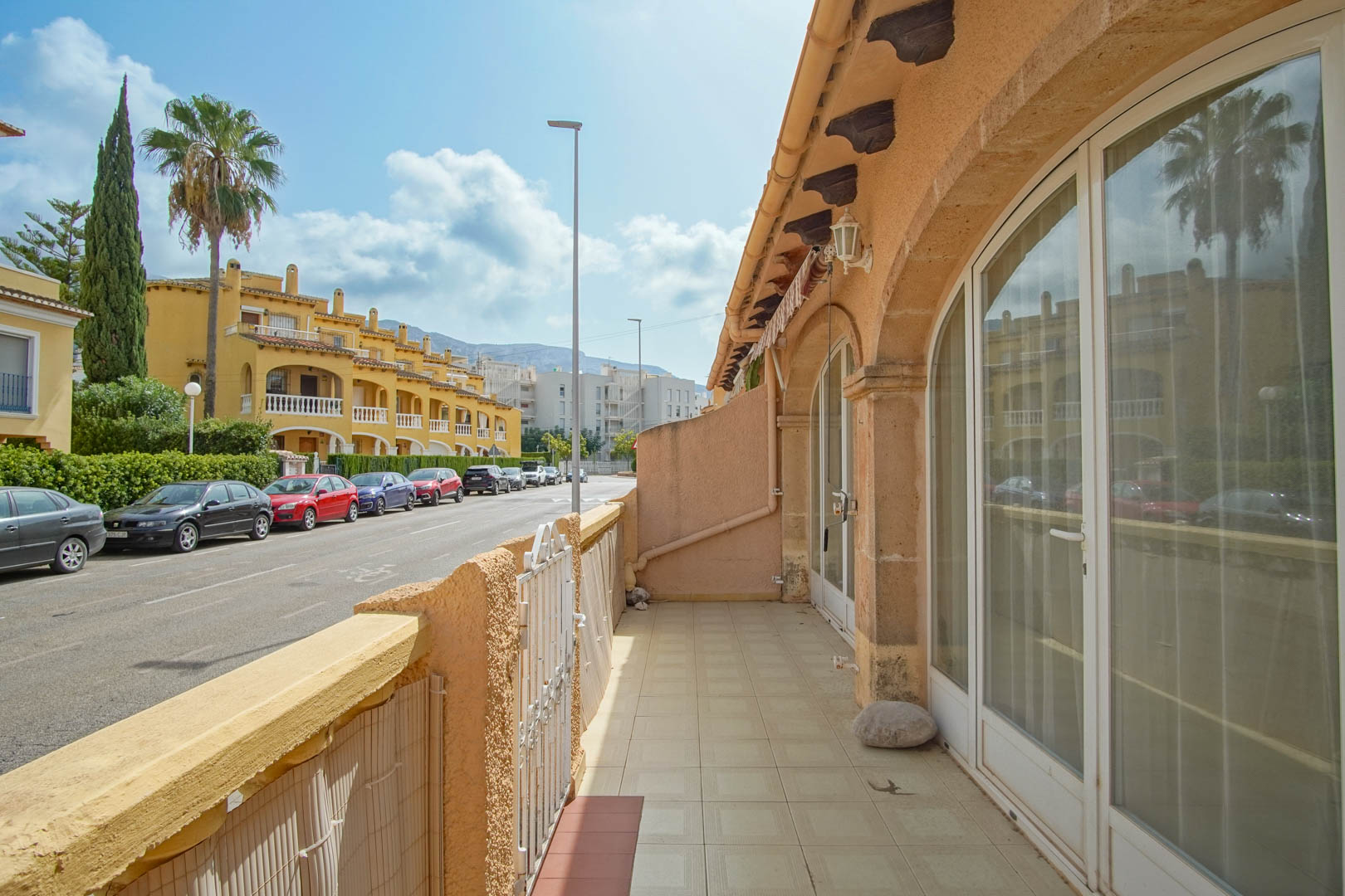 Außen-Terrasse mit Keramikfliesen und großen Rundbogen-Glastüren, die einen Blick auf die Wohnstraße und die mediterrane Umgebung bieten.