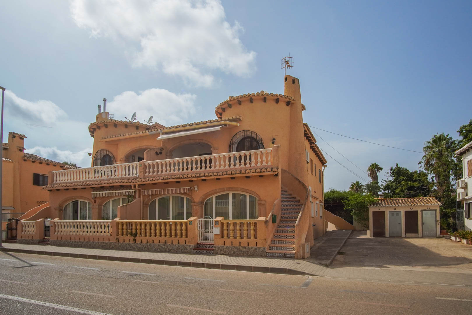 Mediterrane Außenfassade mit Rundbogenfenstern, Steinbalustraden und einer mit Zierfliesen versehenen Außentreppe in Straßennähe.