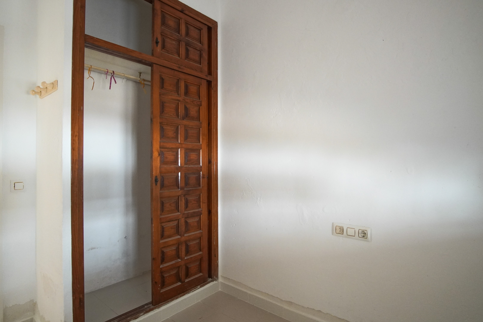 Schlafzimmer mit Einbauschrank aus dunklem Holz und Schiebetüren im Paneel-Design. Strukturierte weiße Wände und Fliesenboden prägen den Raum.