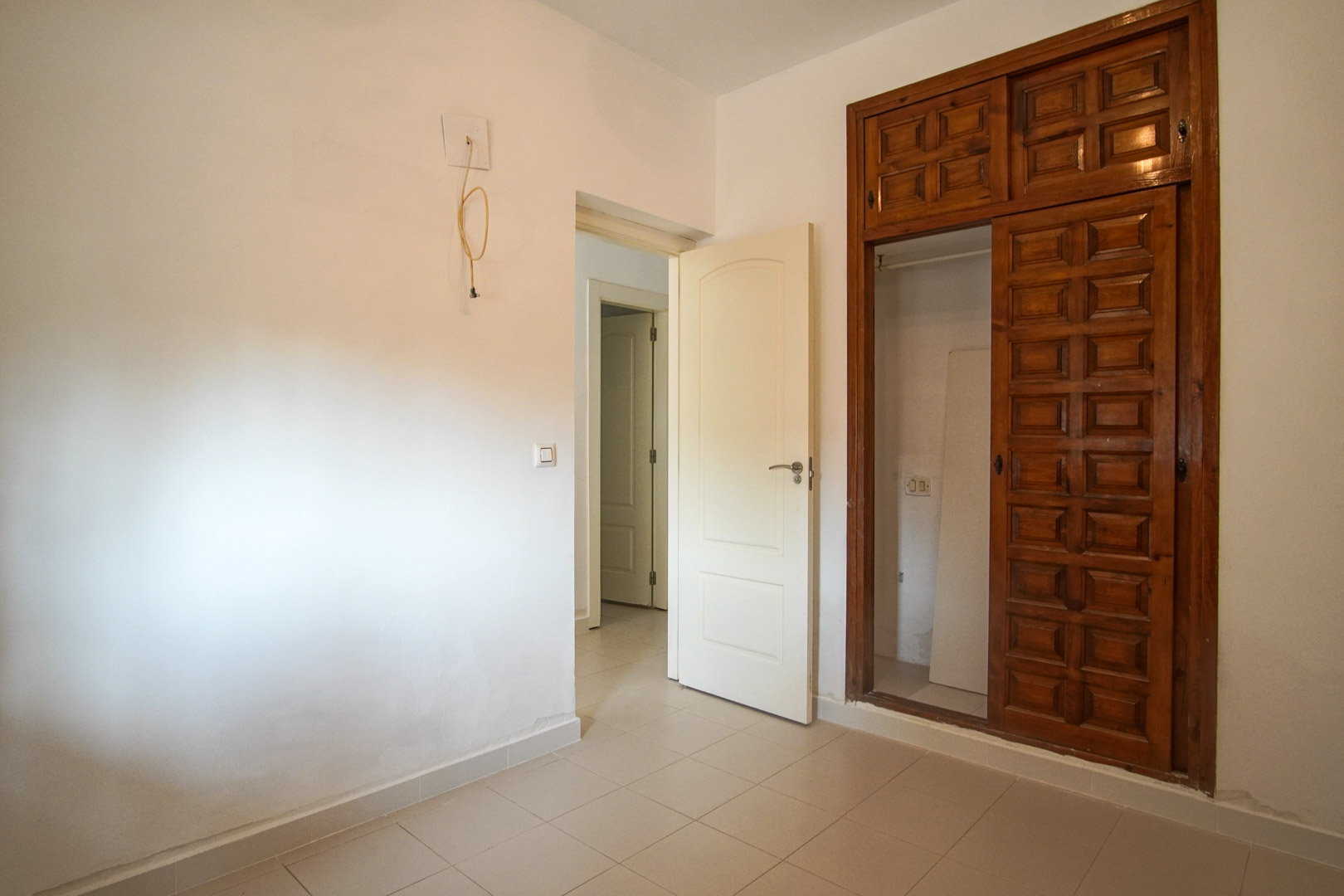 Schlafzimmer mit Einbauschrank aus geschnitztem Holz und Fliesenboden. Der Raum führt zum Flur und bietet Gestaltungsmöglichkeiten durch Renovierung.