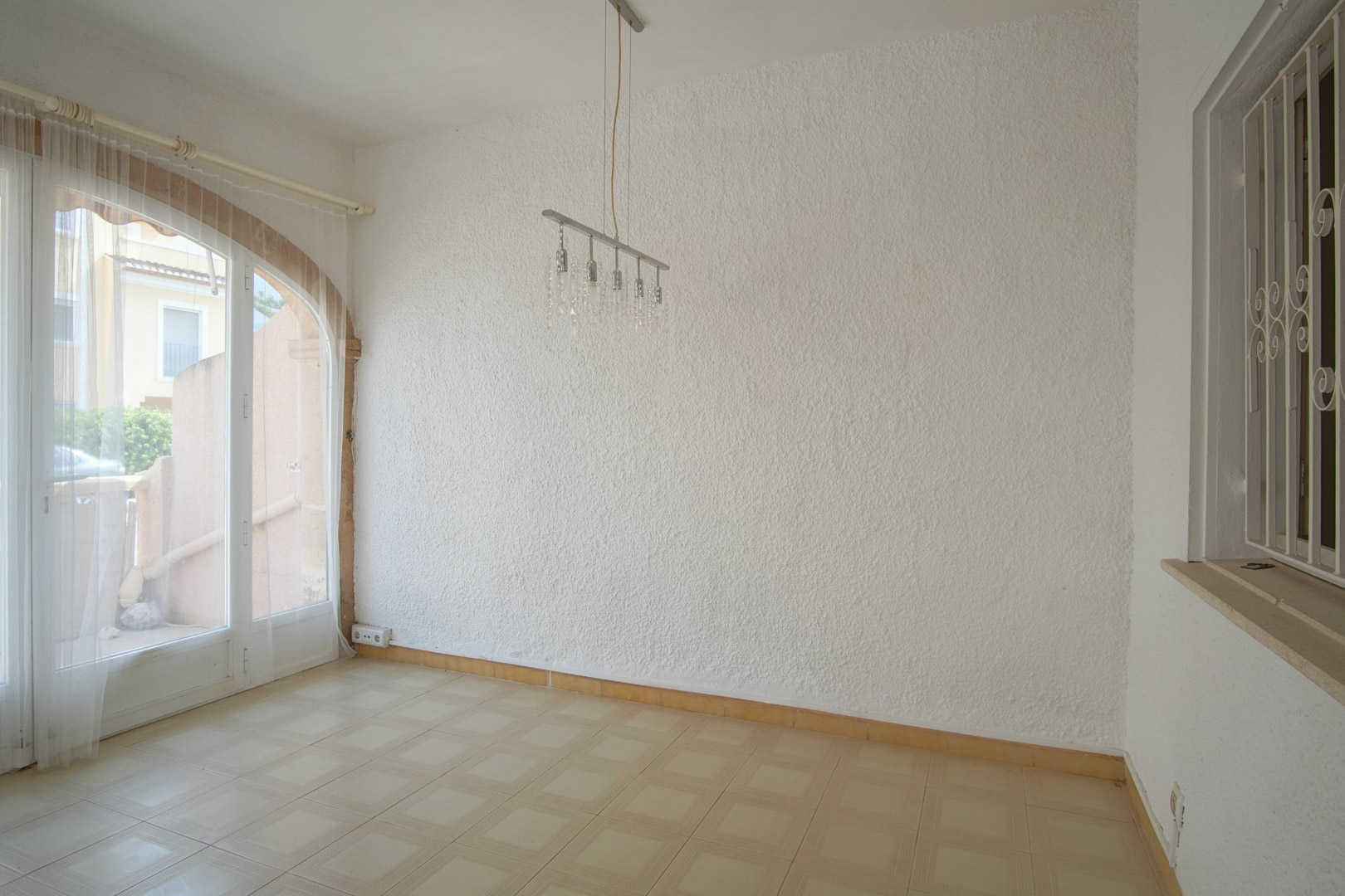 Wohnbereich mit strukturierten Wänden, Fliesenboden und einer bogenförmigen Glastür, die für helles, natürliches Licht sorgt.