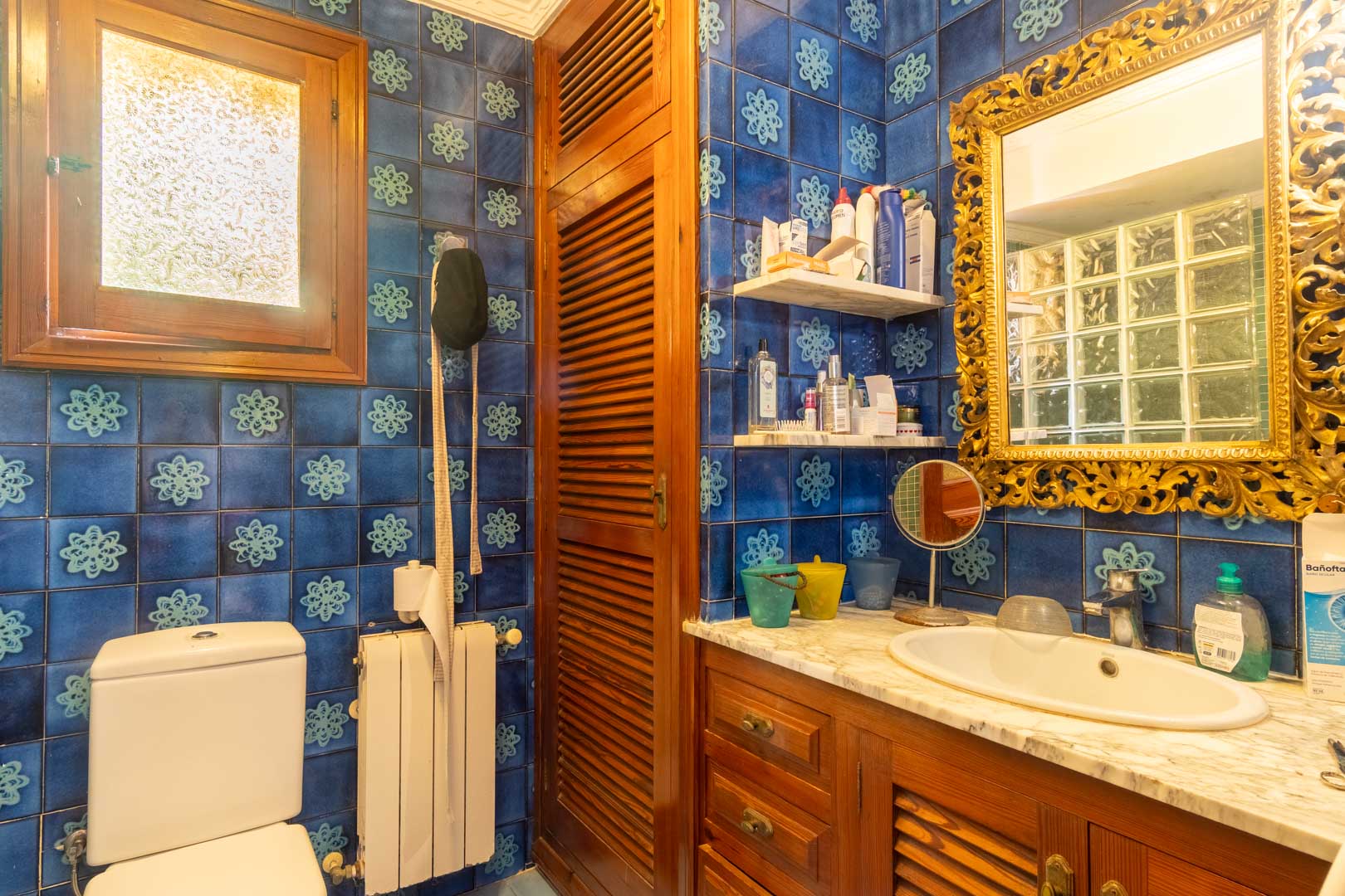 Badezimmer mit blau gemusterten Fliesen, einem Holzwaschtisch mit Marmorplatte und einem prunkvollen goldgerahmten Spiegel im klassischen Stil.