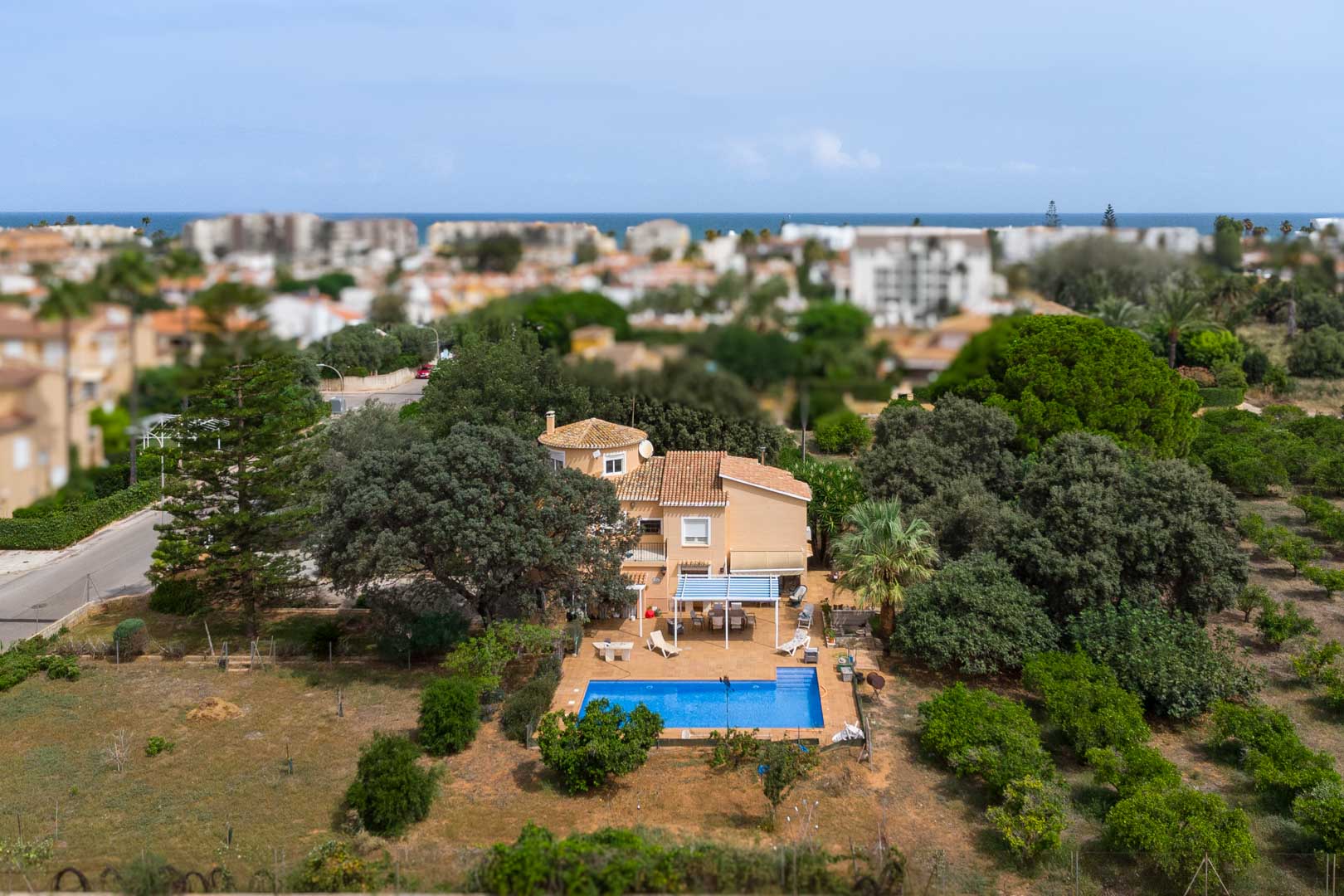 Luftaufnahme der mediterranen Villa in Las Marinas mit großem ebenem Grundstück, Pool, schattigen Terrassen und Meerblick im Hintergrund.
