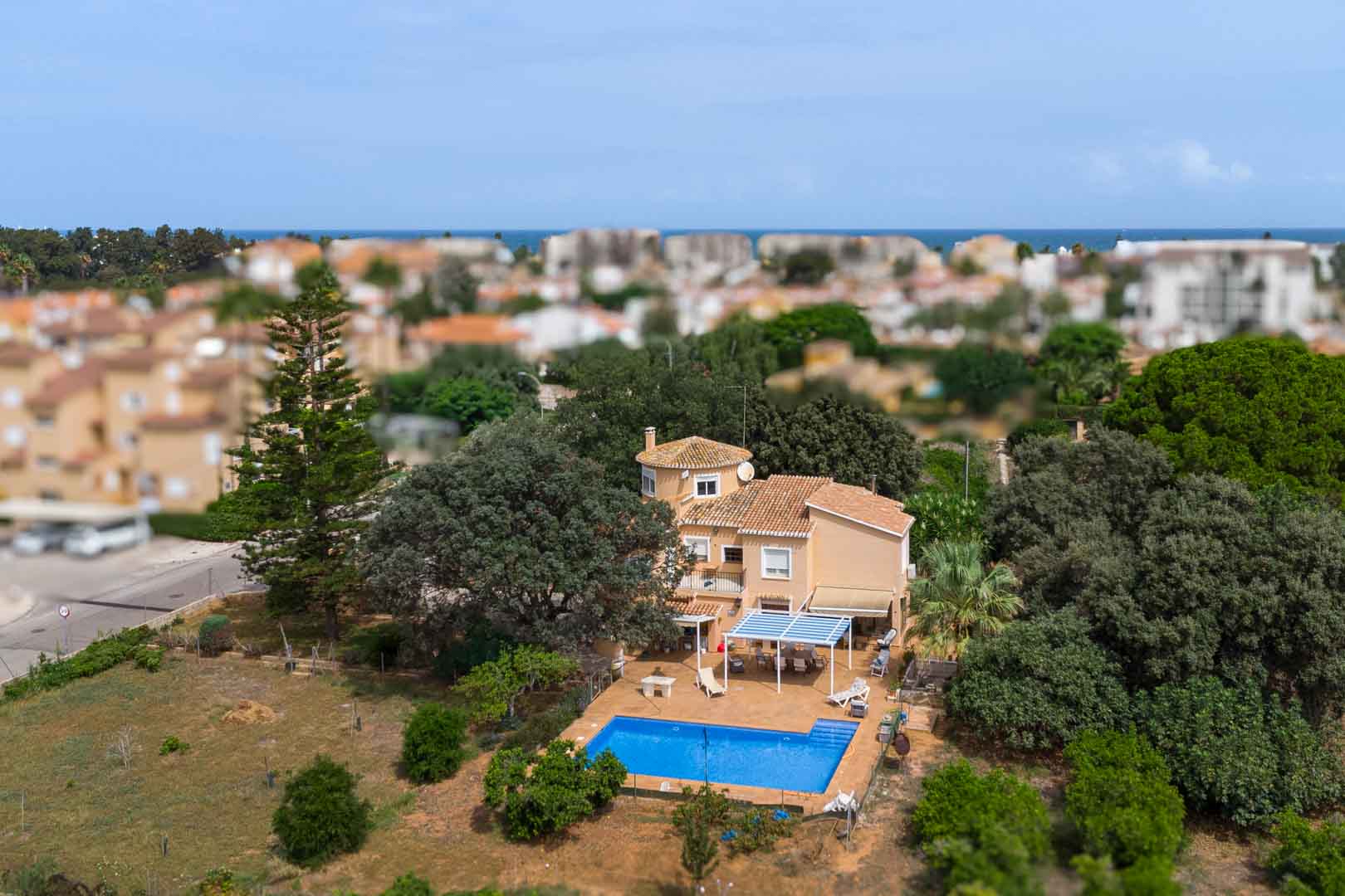 Luftaufnahme der mediterranen Villa mit privatem Pool, schattigen Terrassen und einem weitläufigen, flachen Grundstück mit altem Baumbestand nahe dem Meer.