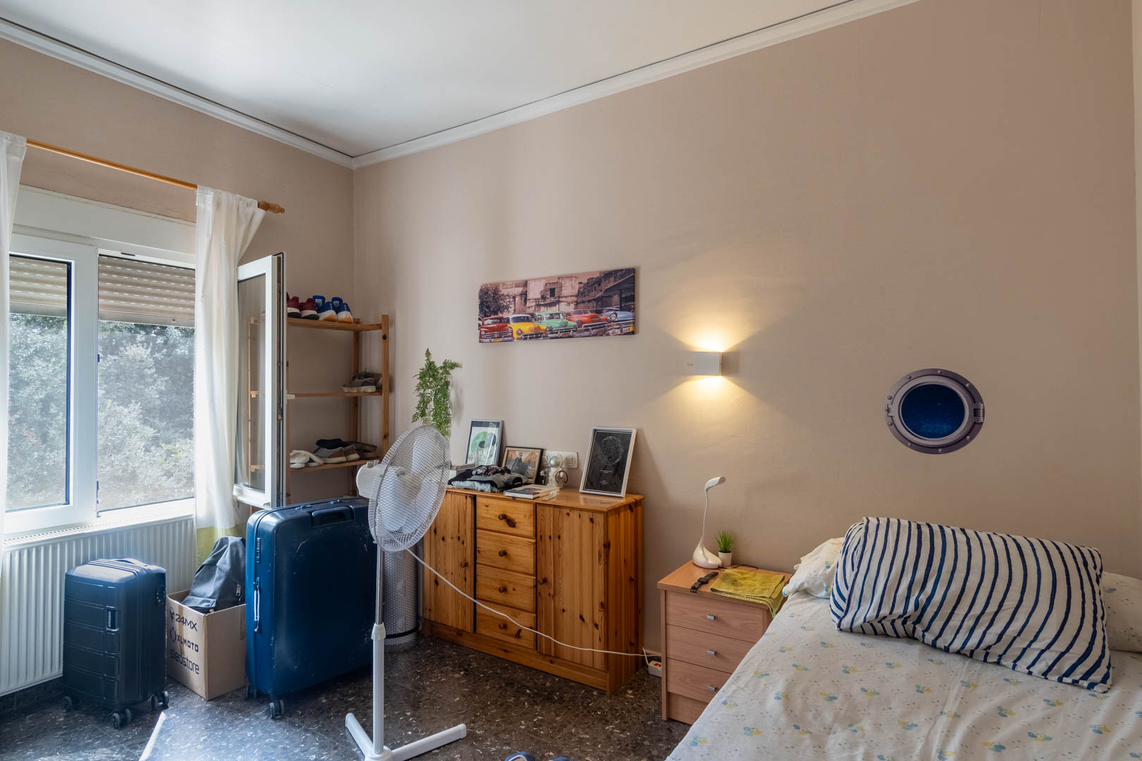 Schlafzimmer mit Terrazzoboden, Naturholzmöbeln und Außenfenster für Tageslicht. Ausgestattet mit Heizkörper und dezenter Wandbeleuchtung.
