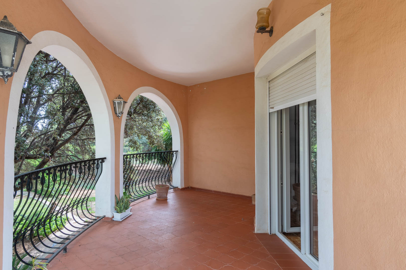 Überdachte Terrasse mit mediterranen Rundbögen, Terrakotta-Fliesenboden und schmiedeeisernem Geländer mit Blick auf den Garten.